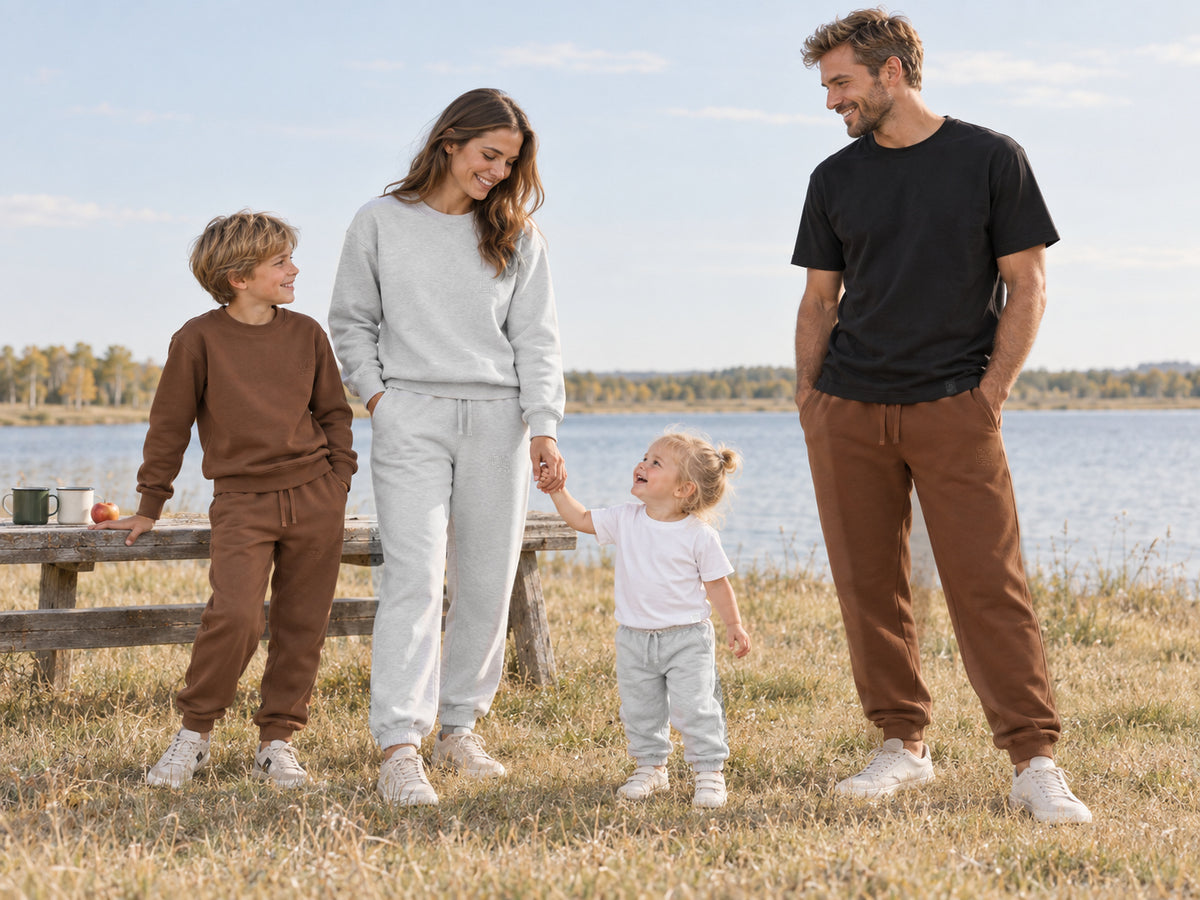 Two adult models, a boy and a toddler girl wearing Motus Gratis cotton clothing at a lakeside picnic.